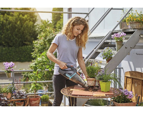 Frau saugt mit einem Akku-Handsauger Erde von einem Gartentisch.
