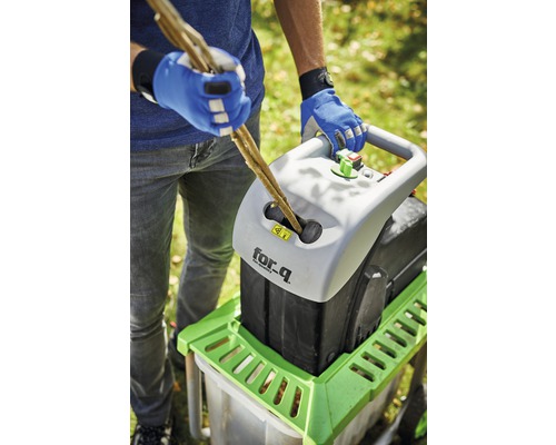 Eine Person führt Äste in einen Häcksler der Marke for_q ein.