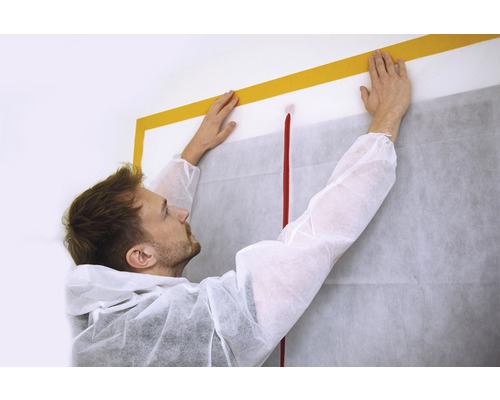 Handwerker befestigt Staubschutzplane mit Klebeband an Wand
