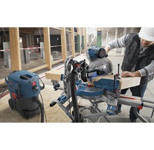 Eine Person bedient eine Kappsäge neben einem Staubsauger in einem Rohbau.