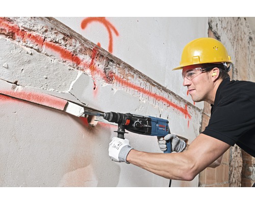 Ein Bauarbeiter bohrt mit einem Bohrhammer ein Loch in eine Wand.