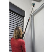 Eine Frau benutzt eine Teleskopbürste zur Reinigung einer Fassade neben einer Regenrinne.