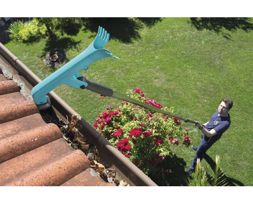 Ein Mann reinigt eine Dachrinne mit einem Dachrinnenreiniger, wobei Laub entfernt wird.