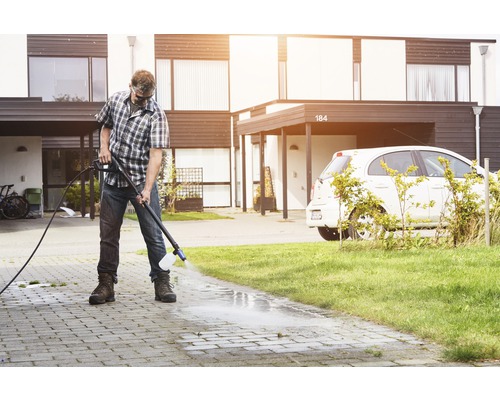 Mann reinigt Auffahrt mit Hochdruckreiniger vor Haus