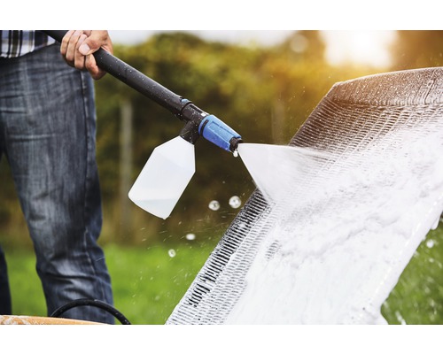 Eine Person reinigt mit einem Hochdruckreiniger ein Möbelstück im Freien.