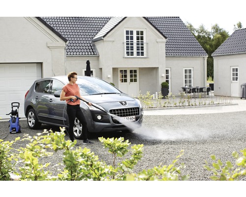 Frau benutzt Hochdruckreiniger zur Autowäsche vor dem Haus