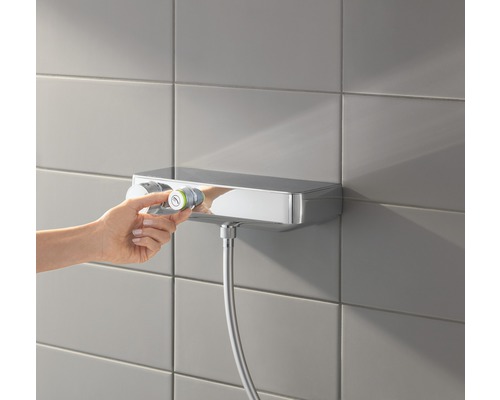 Aufputz-Thermostatbatterie mit Brauseschlauch an einer gefliesten Wand, die Temperatur wird eingestellt.