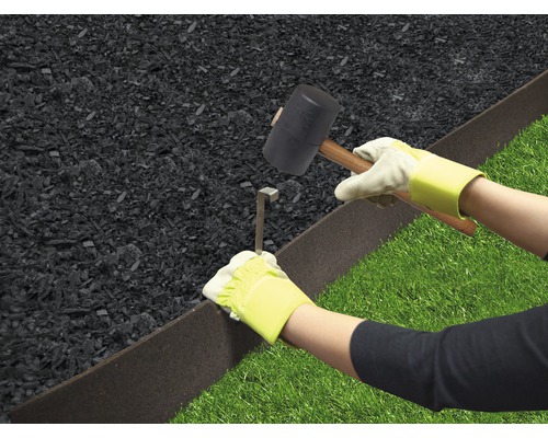Person befestigt Rasenkante mit Hammer und Erdanker zwischen Rasen und Mulch