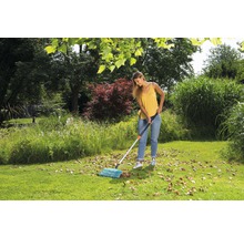 Frau kehrt Laub mit einem Fächerbesen im Garten.