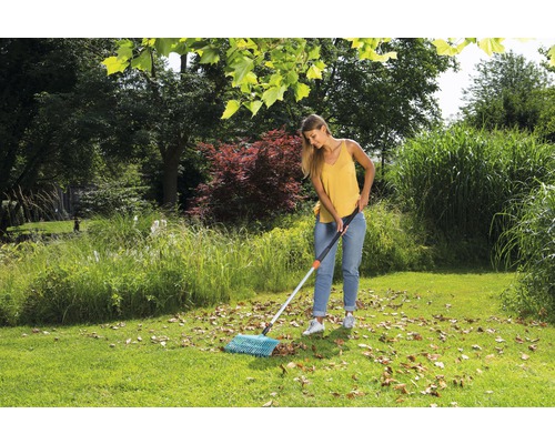 Frau kehrt Laub mit einem Fächerbesen im Garten.