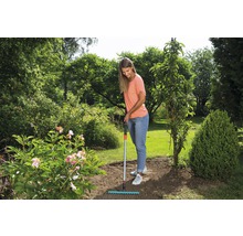 Frau harkt den Boden im Garten mit einem Rechen