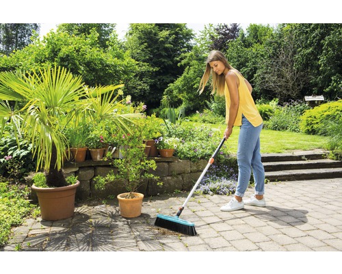 Frau kehrt Steinterrasse mit Straßenbesen in einem Garten