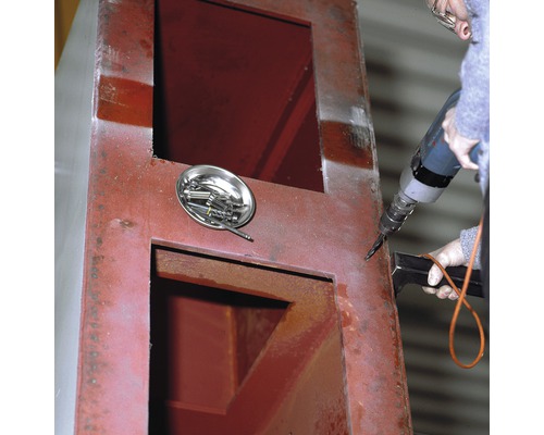 Eine Person bohrt mit einer Bohrmaschine in ein Metallgehäuse. Eine Schale mit Schrauben liegt daneben.