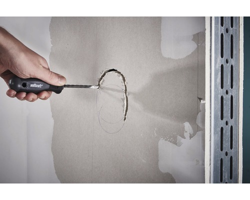 Hand schneidet mit einem Gipskartonschneider ein Loch in eine Gipskartonwand.