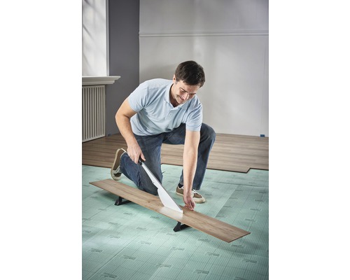 Mann schneidet Laminat mit Laminatschneider auf Trittschalldämmung