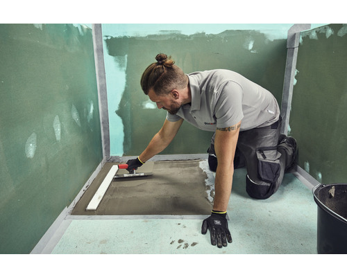 Handwerker, der mit einer Glättkelle Estrich in einem Badezimmer verteilt