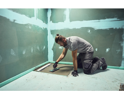 Handwerker bei der Arbeit an einer bodengleichen Dusche mit Spachtel