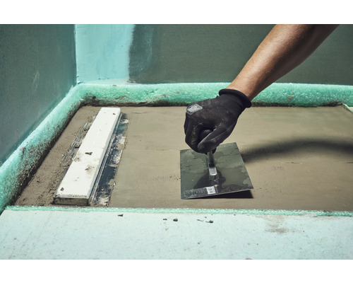 Handwerker bearbeitet Estrich mit einer Glättkelle in einem Badezimmer