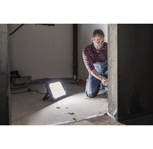 Handwerker bei der Arbeit mit einem LED-Strahler in einem Rohbau