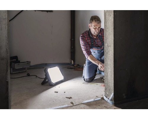 Handwerker bei der Arbeit mit einem LED-Strahler in einem Rohbau