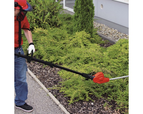 Person schneidet Hecke mit einer elektrischen Heckenschere mit Teleskopstiel