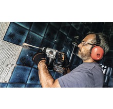 Mann bohrt mit einem Bohrhammer in einer Badezimmerwand mit Fliesen