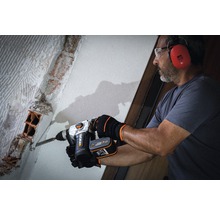 Ein Mann mit Schutzbrille und Gehörschutz arbeitet mit einem Bohrhammer an einer Ziegelwand.