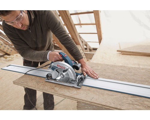 Handwerker schneidet mit einer Handkreissäge ein Holzbrett, unterstützt von einer Führungsschiene. Bosch Logo sichtbar.
