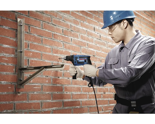 Handwerker bohrt mit einer Schlagbohrmaschine in eine Ziegelwand