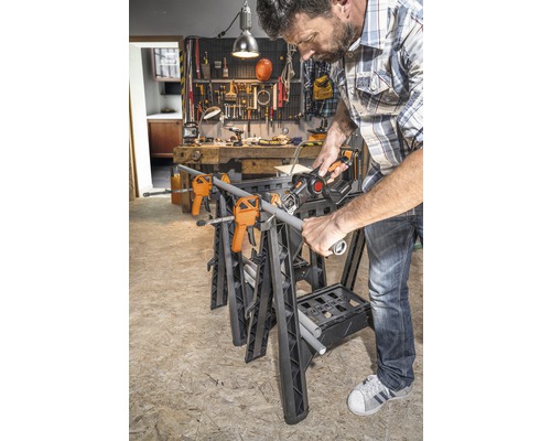 Ein Mann sägt ein Rohr auf einer Werkbank mit Schraubzwingen und einer Säbelsäge in einer Werkstatt.