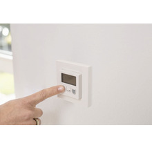 Eine Hand bedient einen elektronischen Raumthermostat an der Wand.