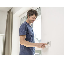 Mann bedient einen Raumthermostat an einer Wand