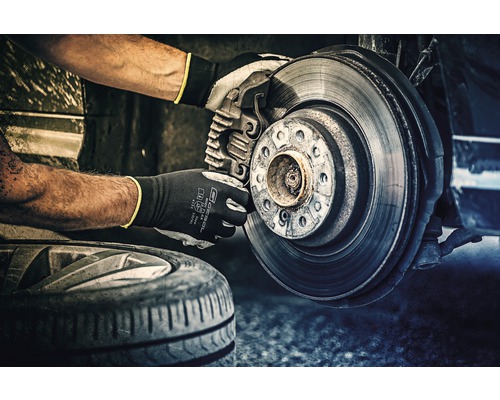 Mechaniker mit Schutzhandschuhen bei der Bremsenreparatur an einem Fahrzeug.