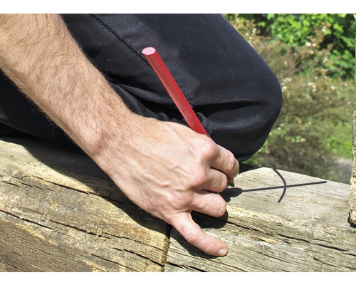 Eine Person zeichnet mit einem Zimmermannsbleistift eine Markierung auf ein Holzstück.