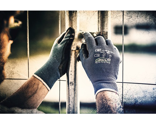 Person mit Arbeitshandschuhen befestigt ein Bauteil an einem Metallzaun