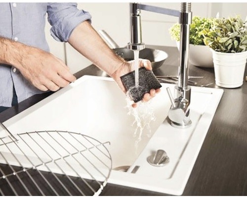 Eine Person reinigt ein Spülbecken mit einem Schwamm unter fließendem Wasser.