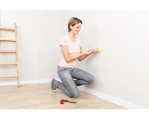 Frau verwendet Dichtstoff aus der Kartusche an einer Wand in einem Raum mit Leiter