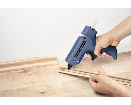 Person klebt Zierleisten mit einer Heißklebepistole.