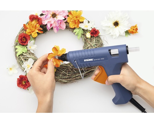 Person klebt Blumen mit Heißklebepistole auf einen Kranz