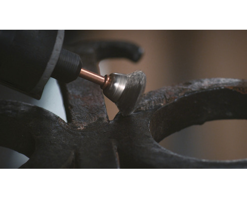 Eine Schleifmaschine mit Drahtbürstenaufsatz schleift eine Metalloberfläche.