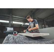 Ein Mann schleift ein Holzbrett mit einem Exzenterschleifer in einer Werkstatt.