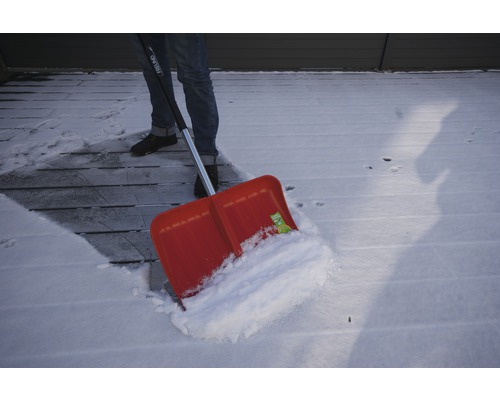 Person schaufelt Schnee mit einer Schneeschaufel von einer Holzterrasse