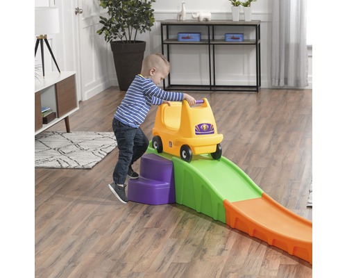 Kind mit gelbem Rutschauto auf Spielzeugachterbahn im Innenraum