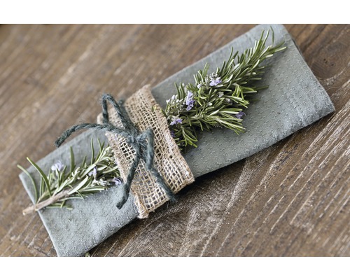 Dekorative Stoffserviette mit Rosmarinzweig und Juteseil auf einem Holztisch.