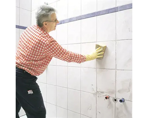 Mann reinigt Fliesen mit einem Schwamm im Badezimmer.