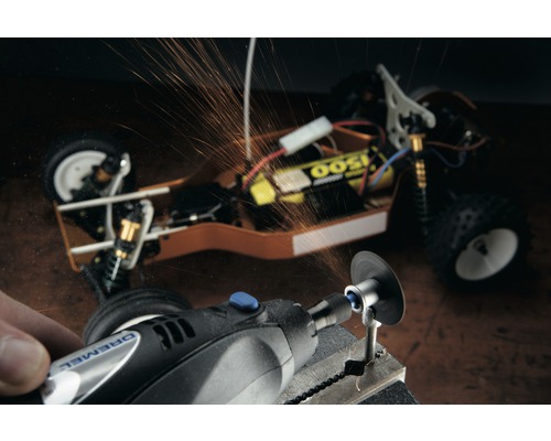 Dremel Logo. Eine Person arbeitet mit einem Dremel Multifunktionswerkzeug an einem Werkstück, Funken fliegen. Im Hintergrund ist ein Modellauto zu sehen.