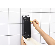 Montage eines Seifenspenders an einer gefliesten Wand mit Bleistiftmarkierung.