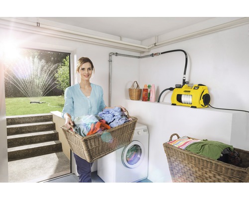 Frau mit Wäschekorb, Waschmaschine und Gartenpumpe im Hauswirtschaftsraum