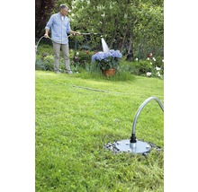 Mann bewässert Blumen mit einem Gartenschlauch und einer Wassersteckdose im Garten