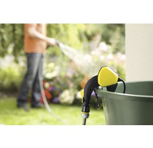 Gartenszene mit Gießstab, der an einem Eimer befestigt ist und eine Person im Hintergrund, die den Garten bewässert.